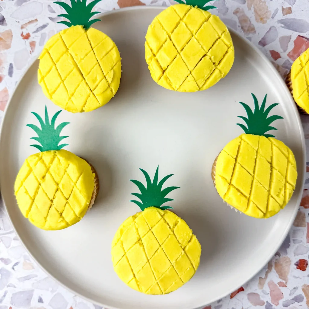 vanilla cupcakes with yellow icing and a green pineapple cake topper