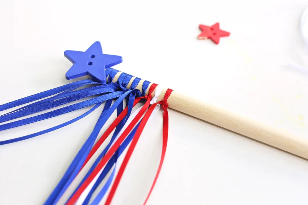 American Flag Wands - Cultivating Brilliant Minds Blue star button attached to a dowel with with blue, red, and white ribbons on a light background.