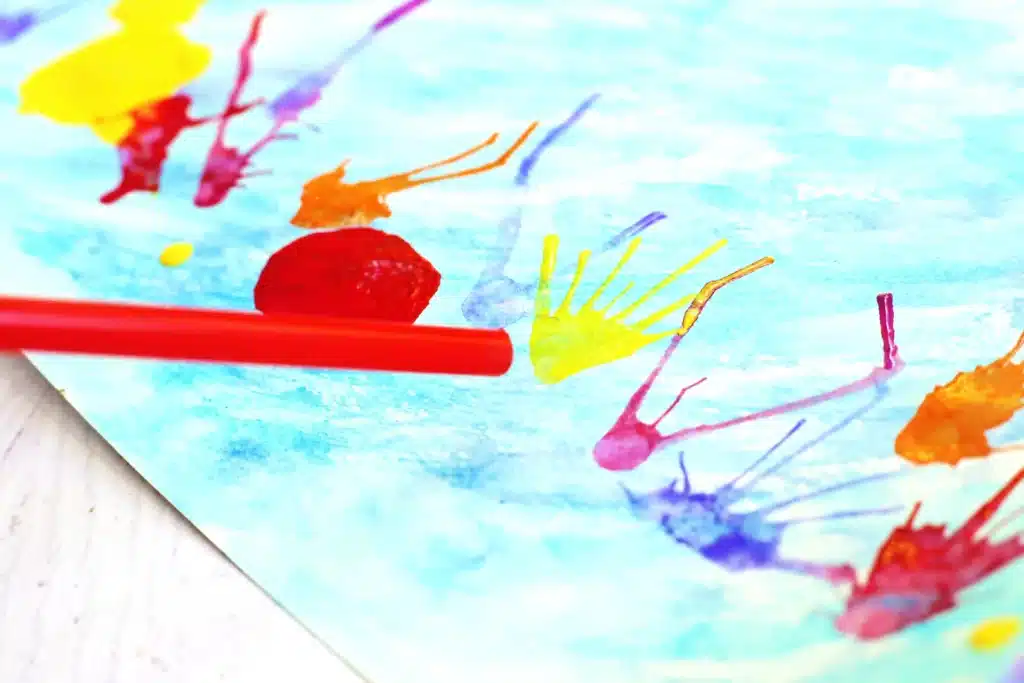 Coral Blow Painting With Straws - Cultivating Brilliant Minds a kid blowing through a straw to move paint