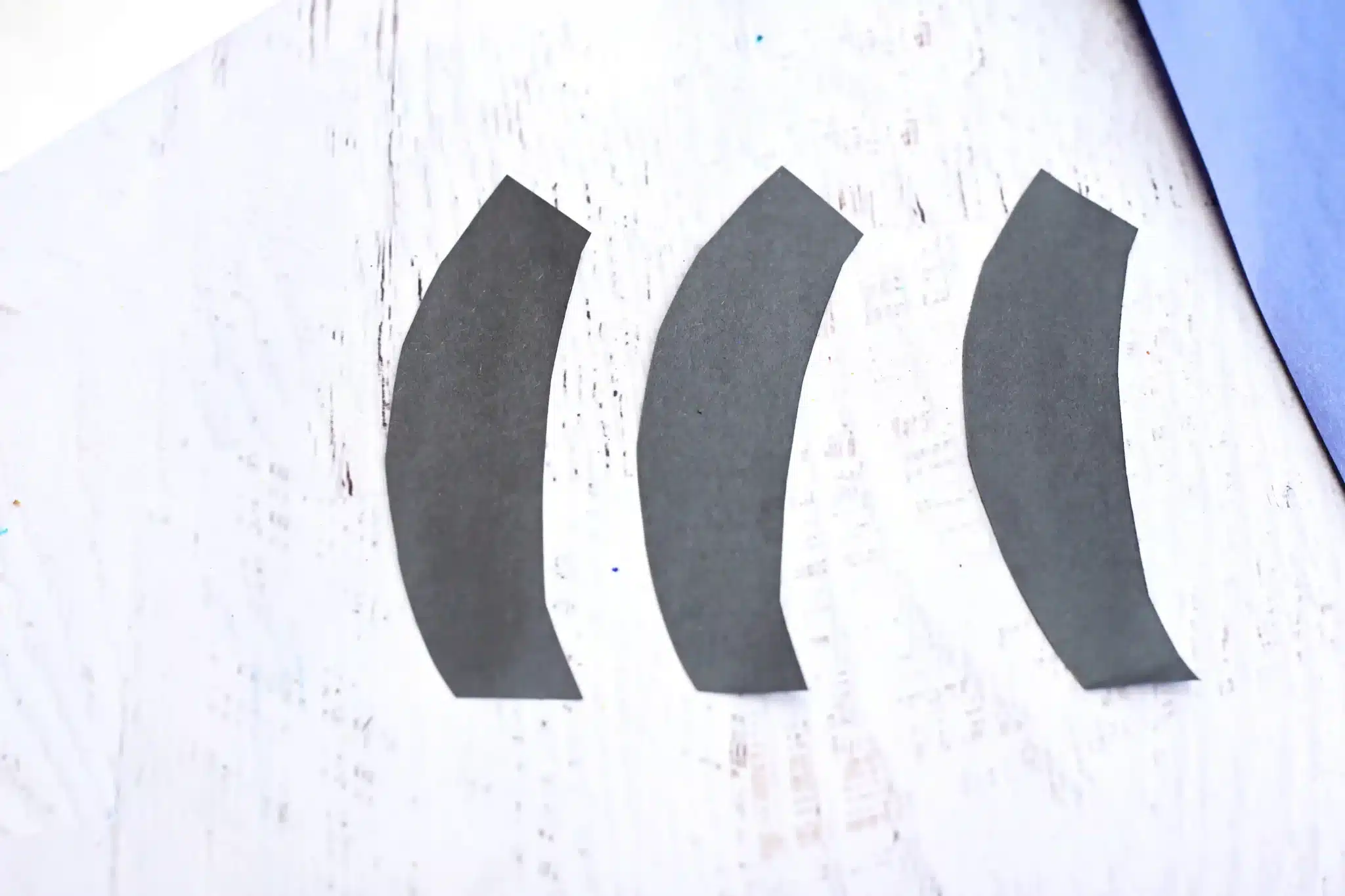 cut black stripes - Cultivating Brilliant Minds Three black curved strips arranged in a row on a light wooden surface, resembling quotation marks.