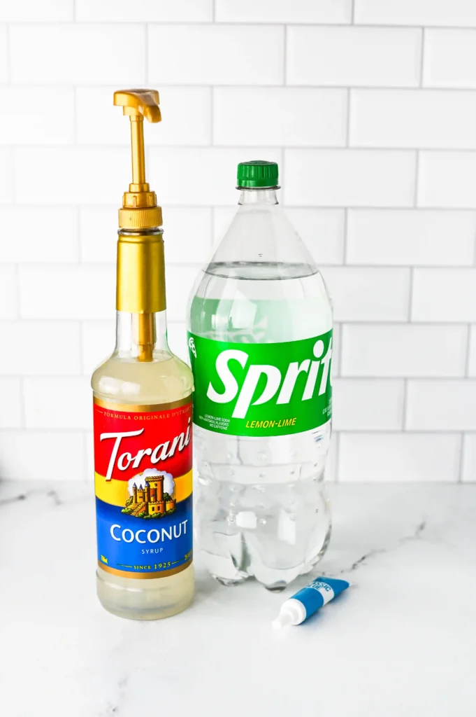 Copycat Sonic Ocean Water - Cultivating Brilliant Minds Torani coconut syrup with a golden pump next to a Sprite lemon-lime bottle on a white tiled counter.