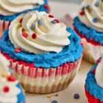 Close-up of red, white, and blue cheesecakes with white frosting, blue frosting accents, and red sprinkles on a white surface.