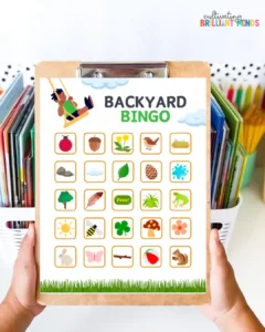Clipboard bingo card titled Backyard Bingo with 20+ small nature icons like leaves, animals, sun, bird, mushroom, etc.