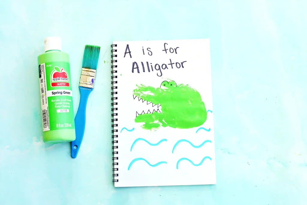 a letter A handprint craft for kids - a notebook with a green handprint stamped on it and decorated with look like an alligator with "A is for Alligator" written on top