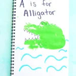 a letter A handprint craft for kids - a notebook with a green handprint stamped on it and decorated with look like an alligator with "A is for Alligator" written on top