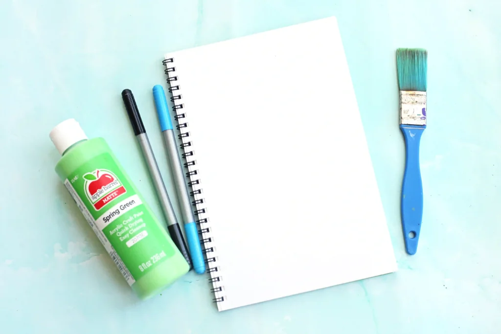 supplies for this alphabet craft for kids - a notebook, green paint, a paint brush, black and blue markers