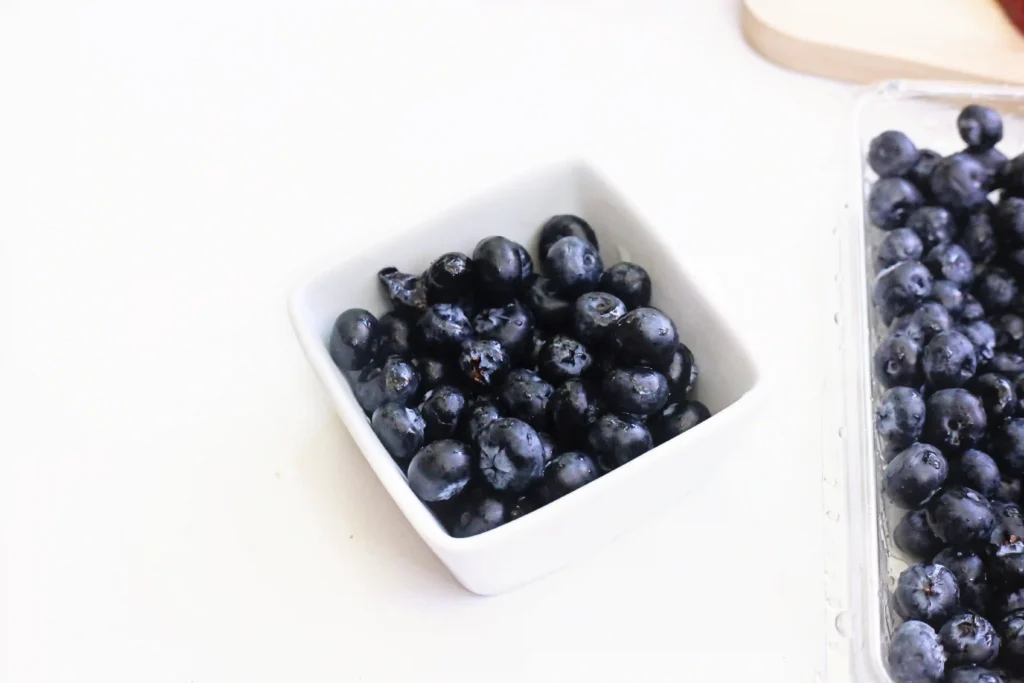Blueberries in a white plastic container on a light surface, with more berries visible in another container to the right.