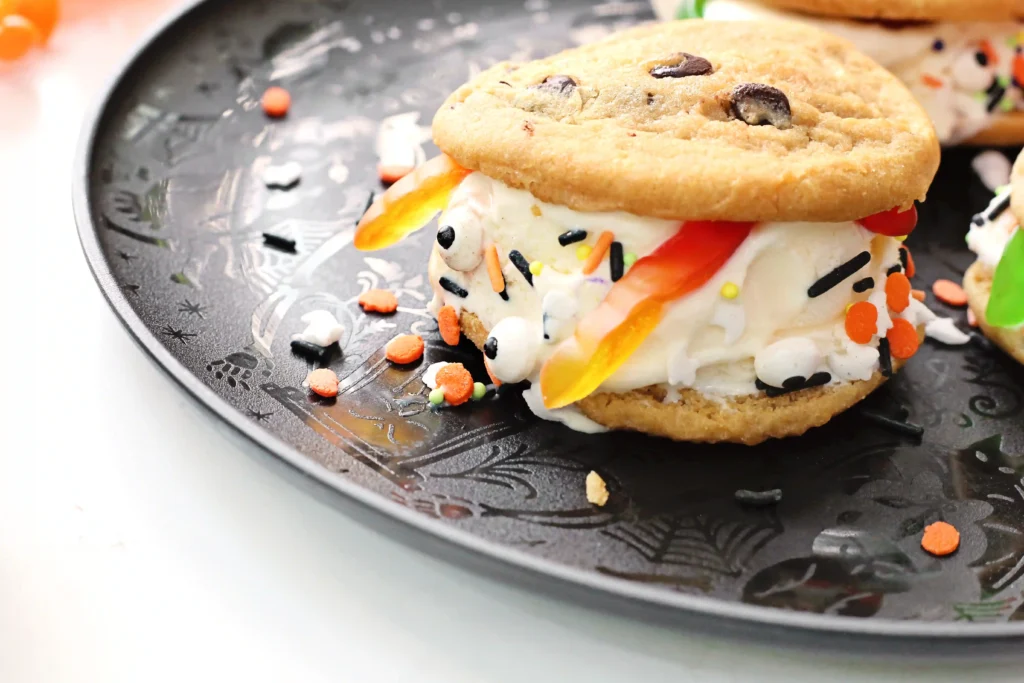 spooky ice cream sandwiches made with chocolate chip cookies, vanilla ice cream, gummy worms, and halloween sprinkles
