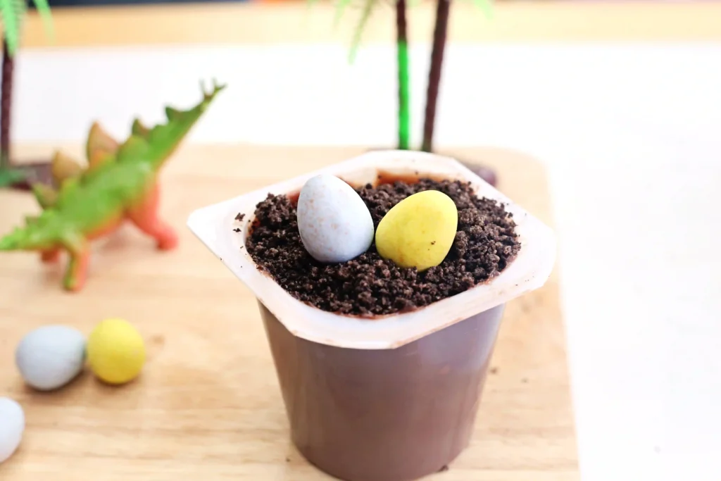 a chocolate pudding cup with crushed oreos on top and two robins eggs