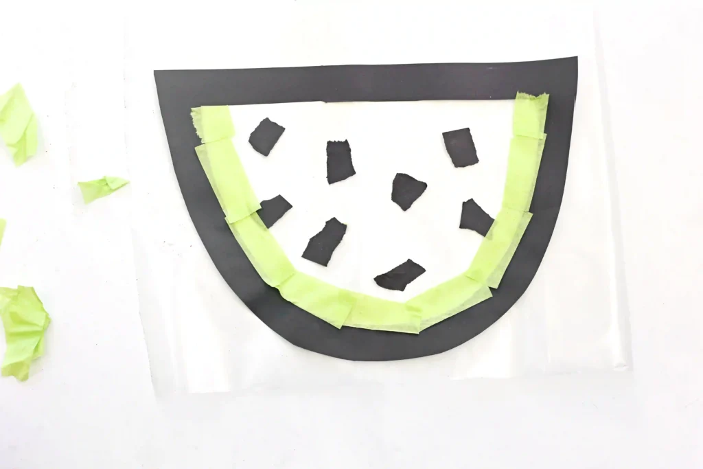 an outline of a watermelon with black construction paper pieces for seeds and agreen tissue paper rind