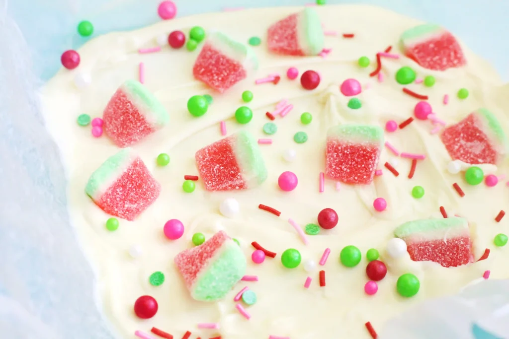 melted White chocolate with pink-green watermelon candy slices and multicolored sprinkles located all over the surface, close-up view.