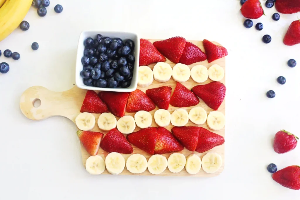 an American Flag Fruit Charcuterie Board that uses blueberries, bananas, and strawberries to make the american flag