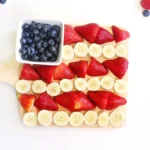 an American Flag Fruit Charcuterie Board that uses blueberries, bananas, and strawberries to make the american flag