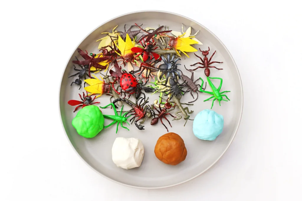 toy bugs and green. white, brown, and blue playdough on a tray