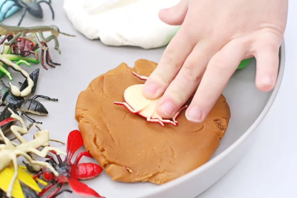 a preschool insect activity of a kid pressing a toy bug into brown playdough