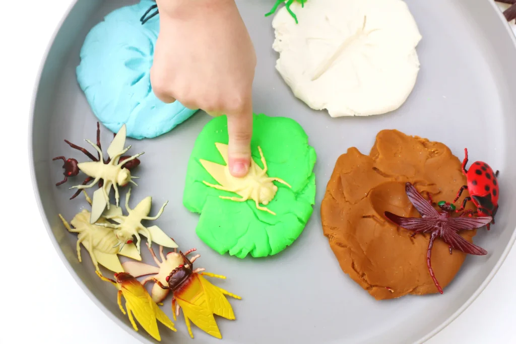a kid pressing a toy bug into green playdough