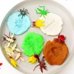 Colorful playdough on a plate with plastic insect toys scattered around.