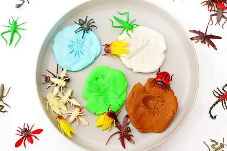 Colorful playdough on a plate with plastic insect toys scattered around.