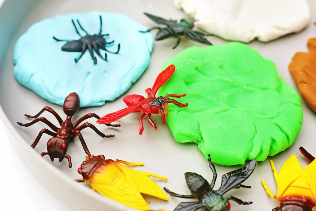 a bug fossils playdough tray with colorful playdough and plastic bugs