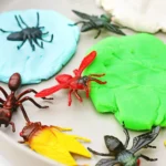 Close-up of colorful toy insects arranged on bright blue and green playdough blobs, part of a craft project.