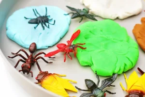 Close-up of colorful toy insects arranged on bright blue and green playdough blobs, part of a craft project.