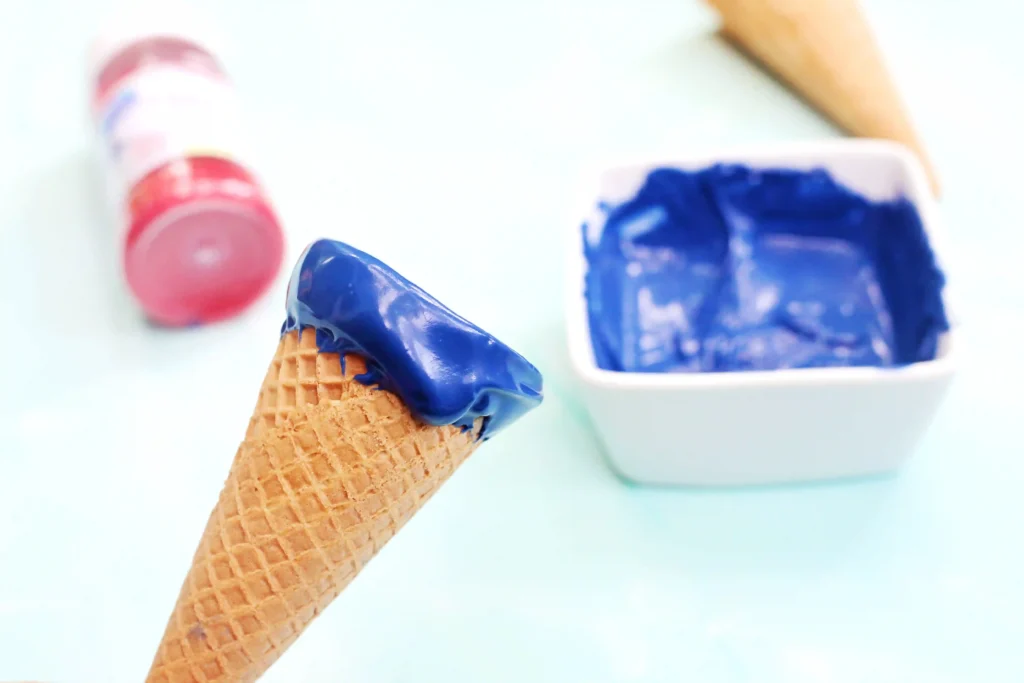 Close-up of a waffle cone with blue candy melts dripping down  on top against a soft, blurred background.