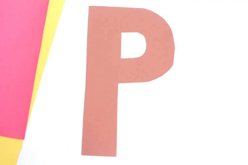 Letter P Pizza Craft - Cultivating Brilliant Minds Close-up of a large brown letter P on a white background, with pink and yellow paper rolled on the left.