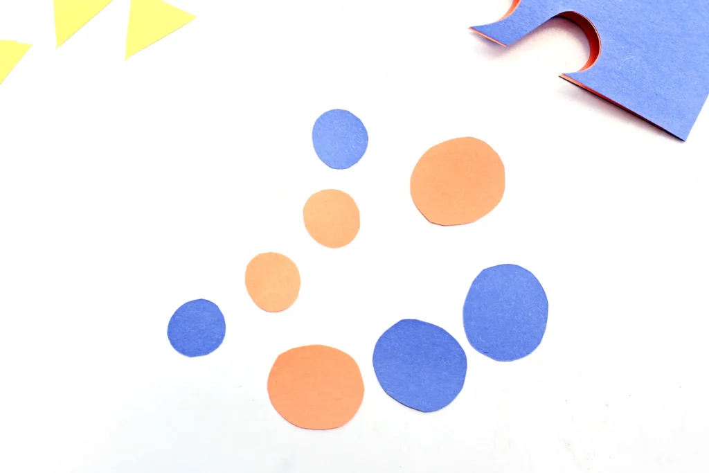 Blue and orange paper cut into circles scattered on a white background, with a blue cut-out piece in the corner.