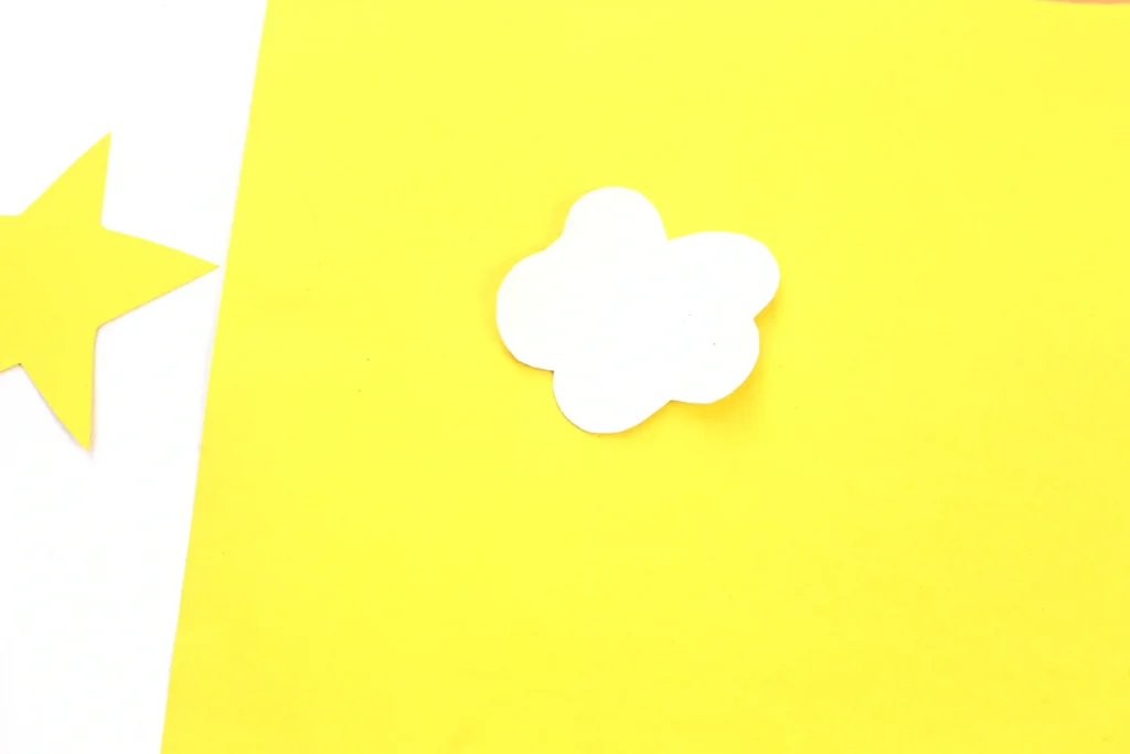 Bright yellow paper background with a white cloud cutout near the center-right and a partial white star shape on the left edge.