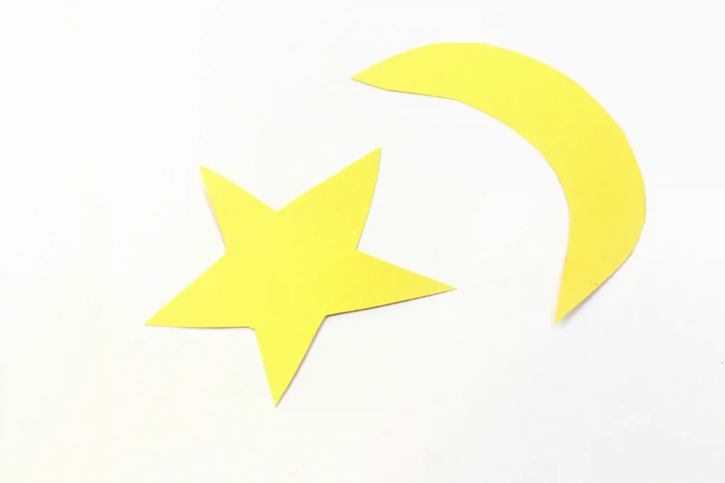 Yellow paper star and a moon on a white background, as if cut from construction paper for a craft project.