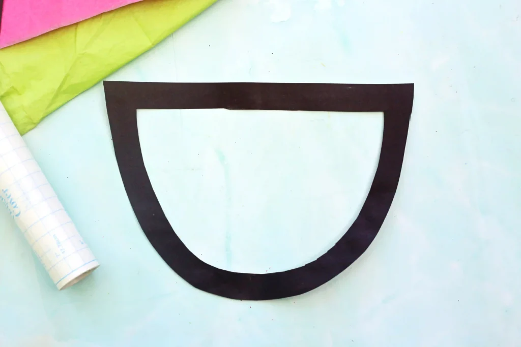 an outline of a watermelon cut out of black construction paper