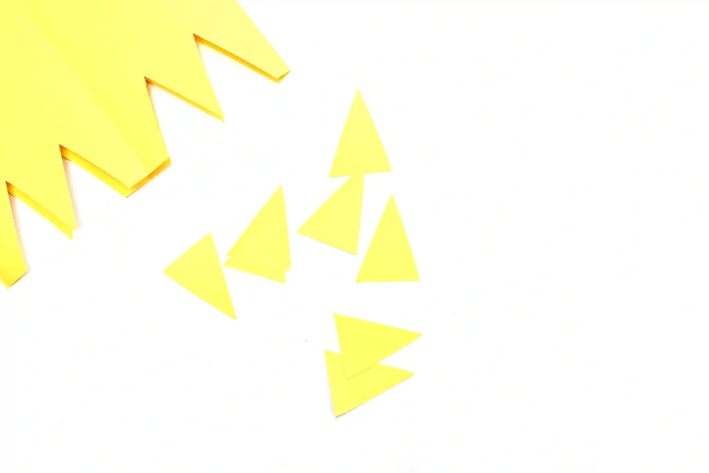 Several yellow triangular paper shapes scattered on a white background so they look like a decorative pattern.