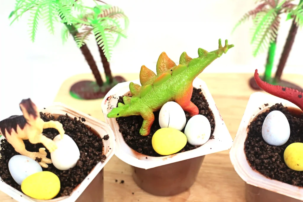dinosaur dirt cups that has chocolate pudding with crushed oreos, robins eggs, and a toy dinosaur on top