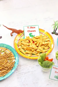 Bright plate of triangular corn chips labeled 'T-Rex Claws' with a small green dinosaur nearby.