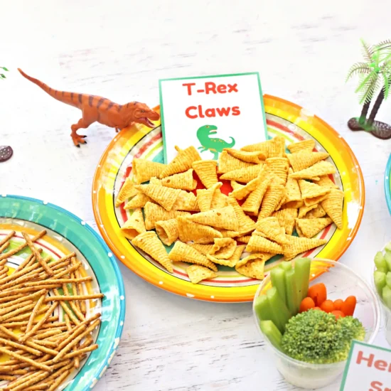 Bright plate of triangular corn chips labeled 'T-Rex Claws' with a small green dinosaur nearby.
