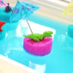 a toy dinosaur on a slice of a pool noodle with a mini umbrella in blue water