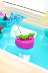 a toy dinosaur on a slice of a pool noodle with a mini umbrella in blue water