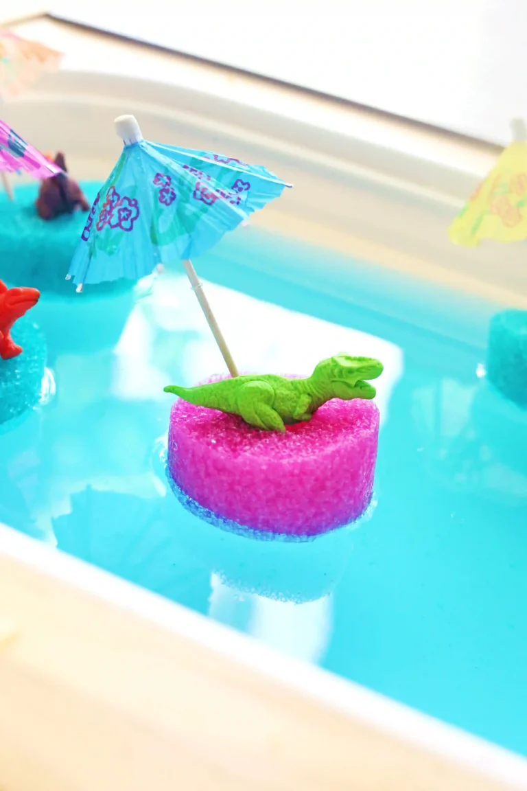 a toy dinosaur on a slice of a pool noodle with a mini umbrella in blue water