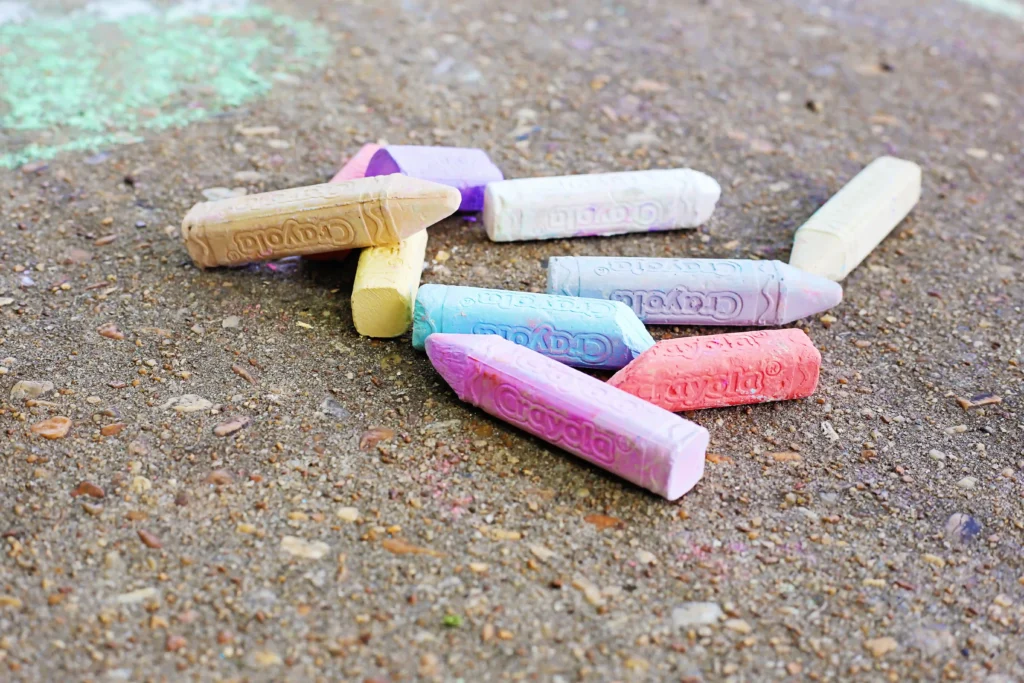 Pastel-colored sidewalk chalk sticks scattered on a rough pavement surface.
