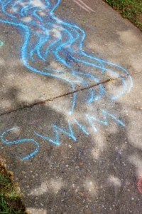 Blue chalk scribbles on a concrete sidewalk forming looping, wavy lines.