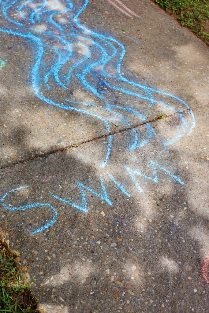 Blue chalk scribbles on a concrete sidewalk forming looping, wavy lines.