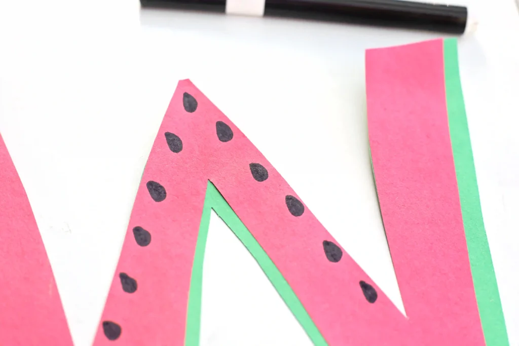 a letter craft for preschoolers of a letter W cut out of red and green construction paper with black seeds drawn on