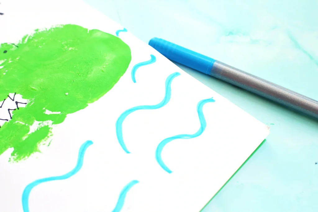 a preschool art activity with a green handprint decorated to look like an alligator in water