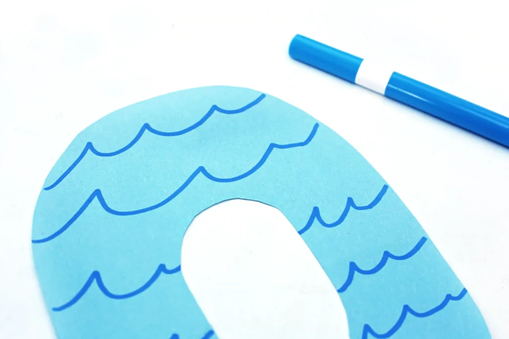 Close-up of a blue letter o paper cutout with wavy lines on a white background; a blue marker sits nearby.