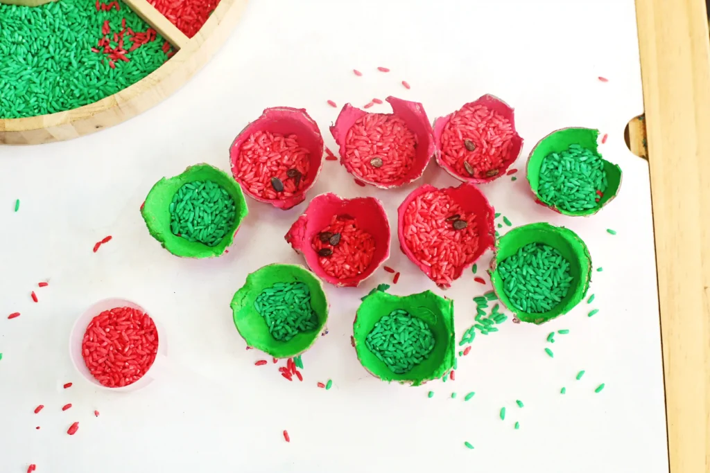 colored red and green egg carton cups filled with colored rice on a white surface.