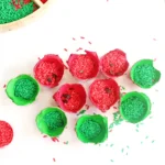 Colorful red and green rice grains in painted egg carton cups arranged on a white surface, with a wooden tray in the corner and scattered pieces around.