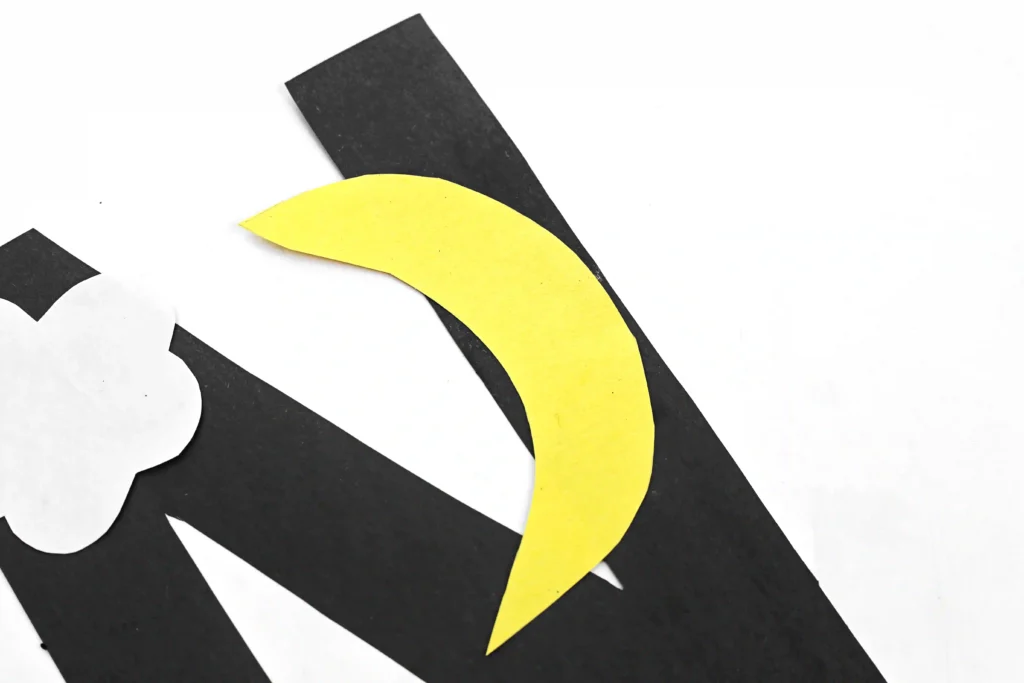 a letter n cut out of black construction paper with a white cloud and yellow moon glued to it