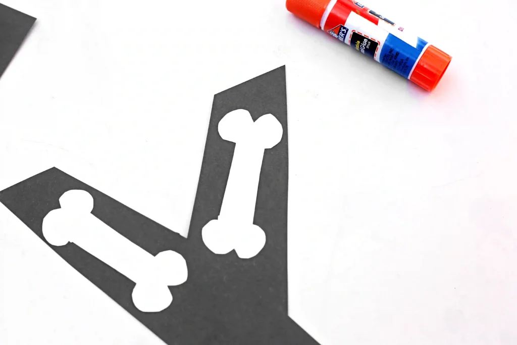 a letter x cut out of black construction paper with white construction paper bones glued on