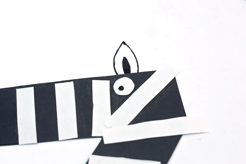 a black letter z cut out of construction paper with white paper strips, an eye, and an ear glued on to look like a zebra for this letter craft for preschoolers