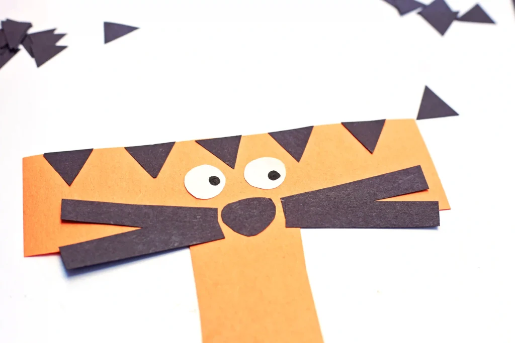a t is for tiger paper craft that has a letter t cut out of orange construction paper with black triangles for stripes and eyes, a nose, and whiskers